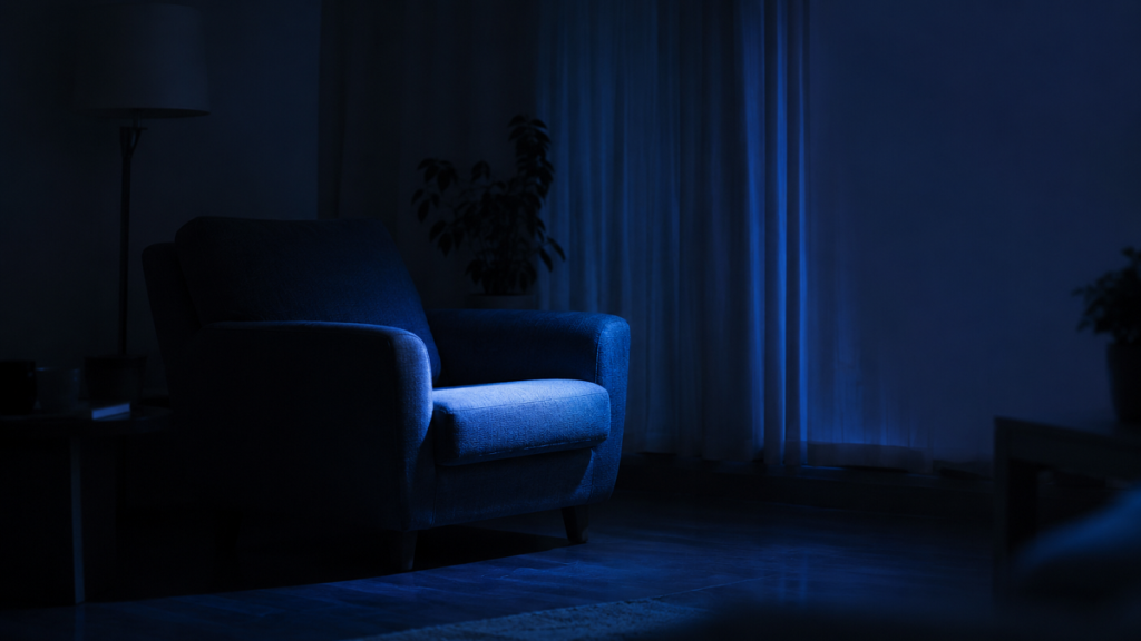An empty armchair lit by the cold blue glow of an unseen screen at night
