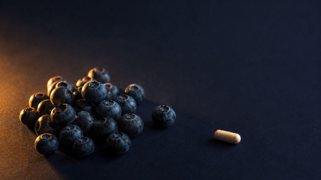 Heap of fresh blueberries beside a single capsule on a dark surface
